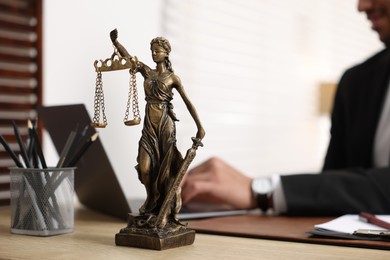 Photo of Lawyer working with laptop at table in office, focus on statue of Lady Justice