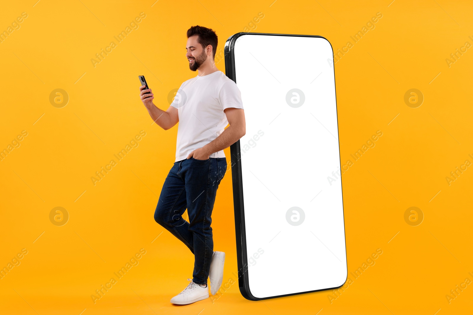 Image of Man with mobile phone standing near huge device with empty screen on dark beige background. Mockup for design