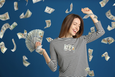 Happy young woman with dollars under money rain on blue background