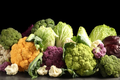 Photo of Different fresh cabbages on table against black background. Healthy food