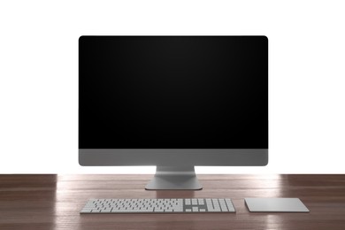 Photo of Modern computer with blank monitor screen and peripherals on wooden table against white background