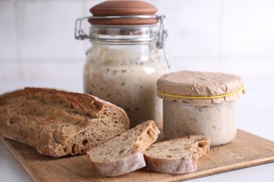 Photo of Sourdough starter in glass jars and fresh bread on light table