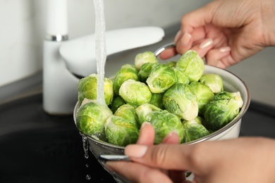 Photo of Woman washing Brussels sprouts with running water over sink, closeup