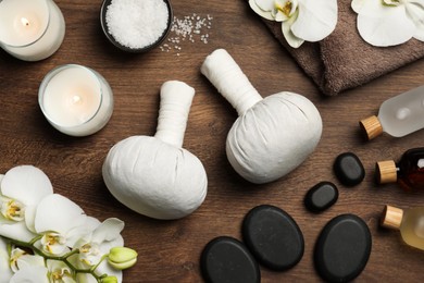 Flat lay composition with herbal massage bags and other spa products on wooden table