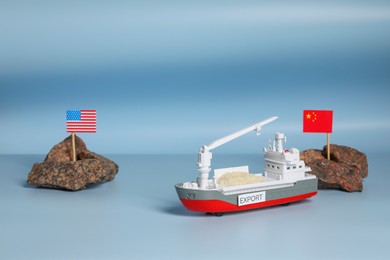 Photo of Toy cargo vessel, stones with American and Chinese flags on color background. Export concept