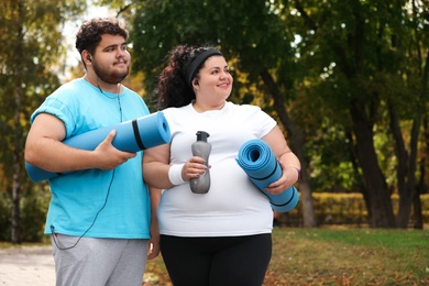 Overweight couple wearing sportswear with mats in park