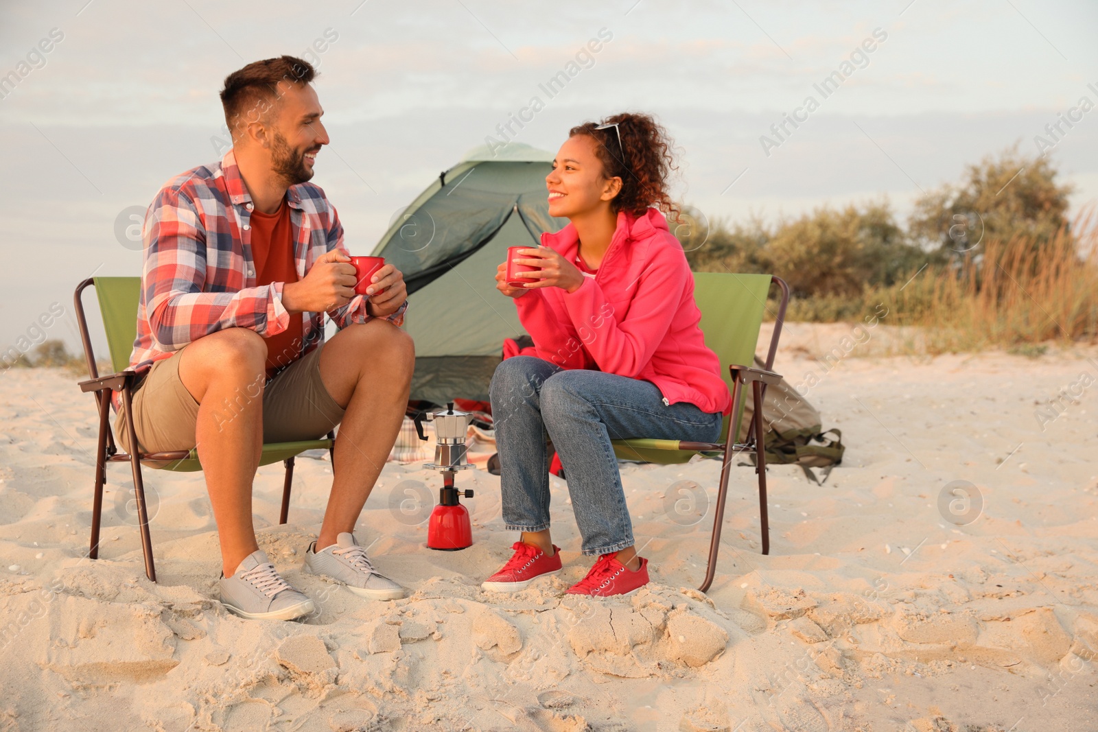 Photo of Couple with hot drinks on beach near camping tent