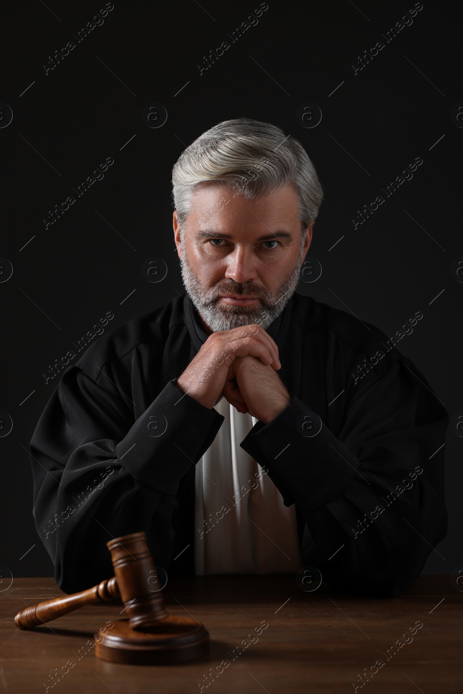 Photo of Judge with gavel sitting at wooden table against black background