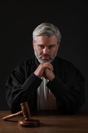 Photo of Judge with gavel sitting at wooden table against black background