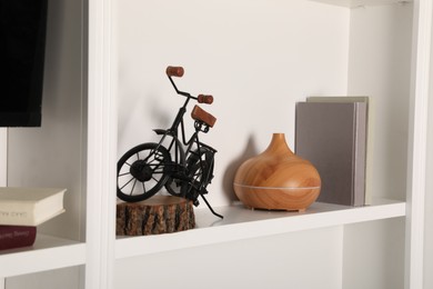 Photo of White shelf with books, air humidifier and bicycle figure indoors. Interior design