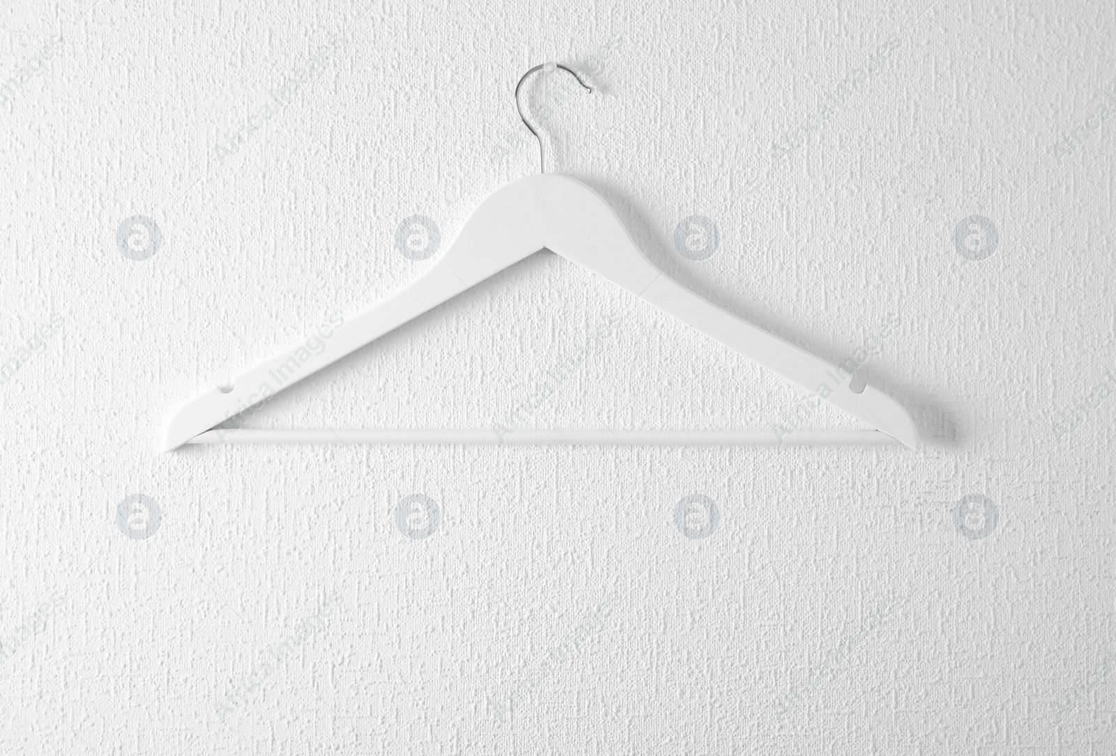 Photo of Empty clothes hanger on light wall. Wardrobe accessory