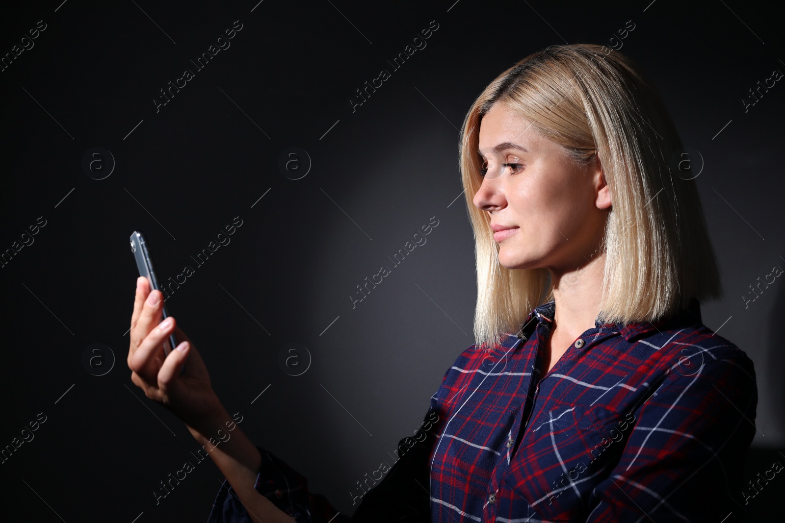 Photo of Woman using facial detection system of modern smartphone on dark background