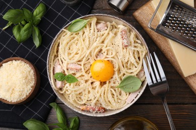 Photo of Bowl of tasty pasta Carbonara with basil leaves and egg yolk on wooden table, flat lay