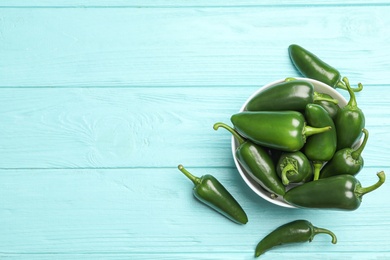 Photo of Bowl with green hot chili peppers on light blue wooden table, flat lay. Space for text