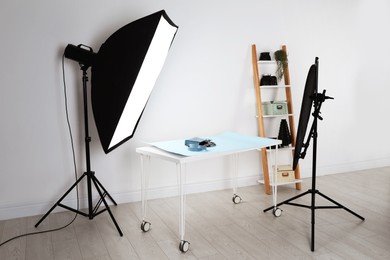 Photo of Professional lighting equipment near table with fashionable women's accessories in photo studio