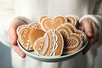 Photo of Woman holding plate with tasty heart shaped gingerbread cookies, closeup