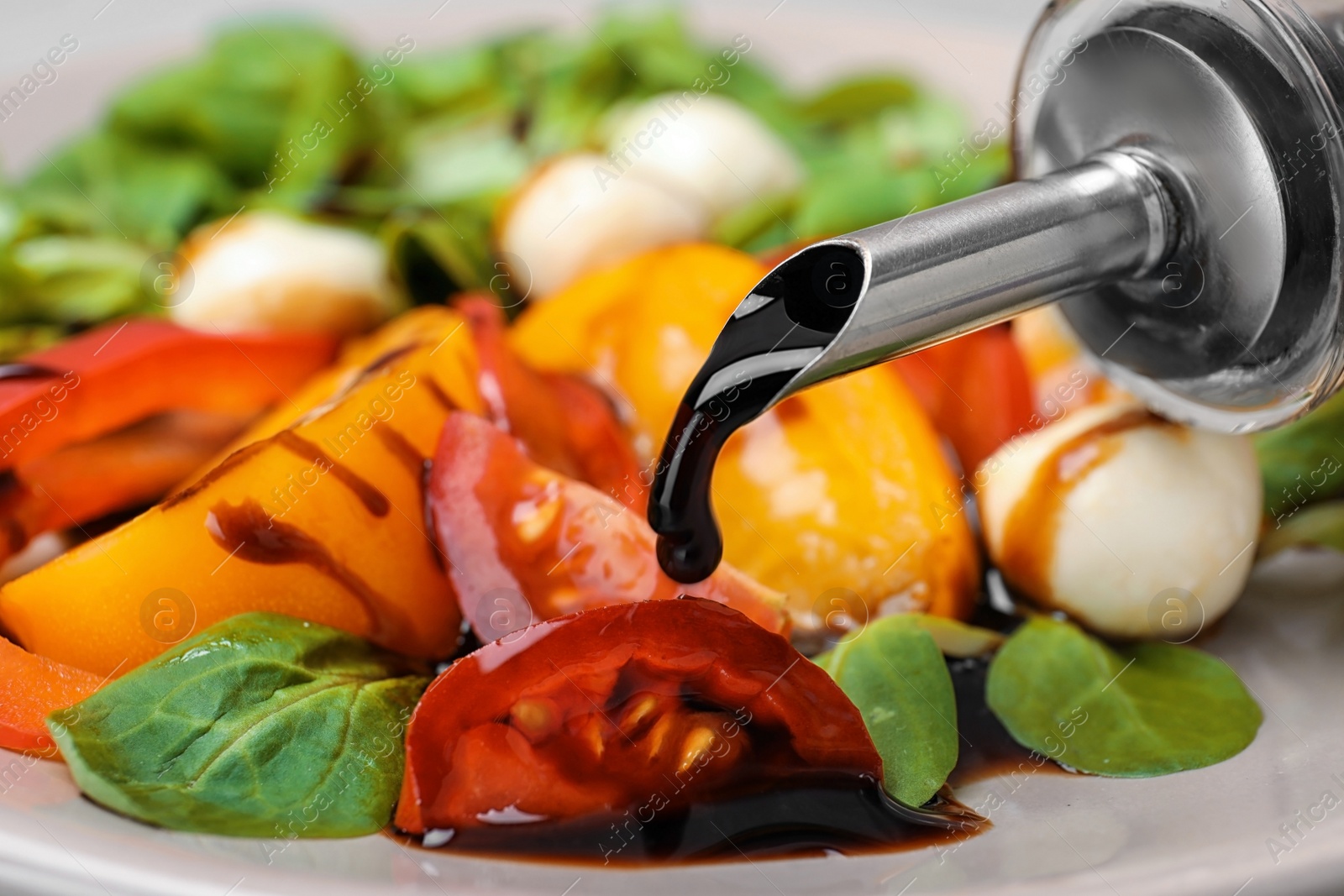 Photo of Pouring balsamic vinegar onto vegetable salad, closeup