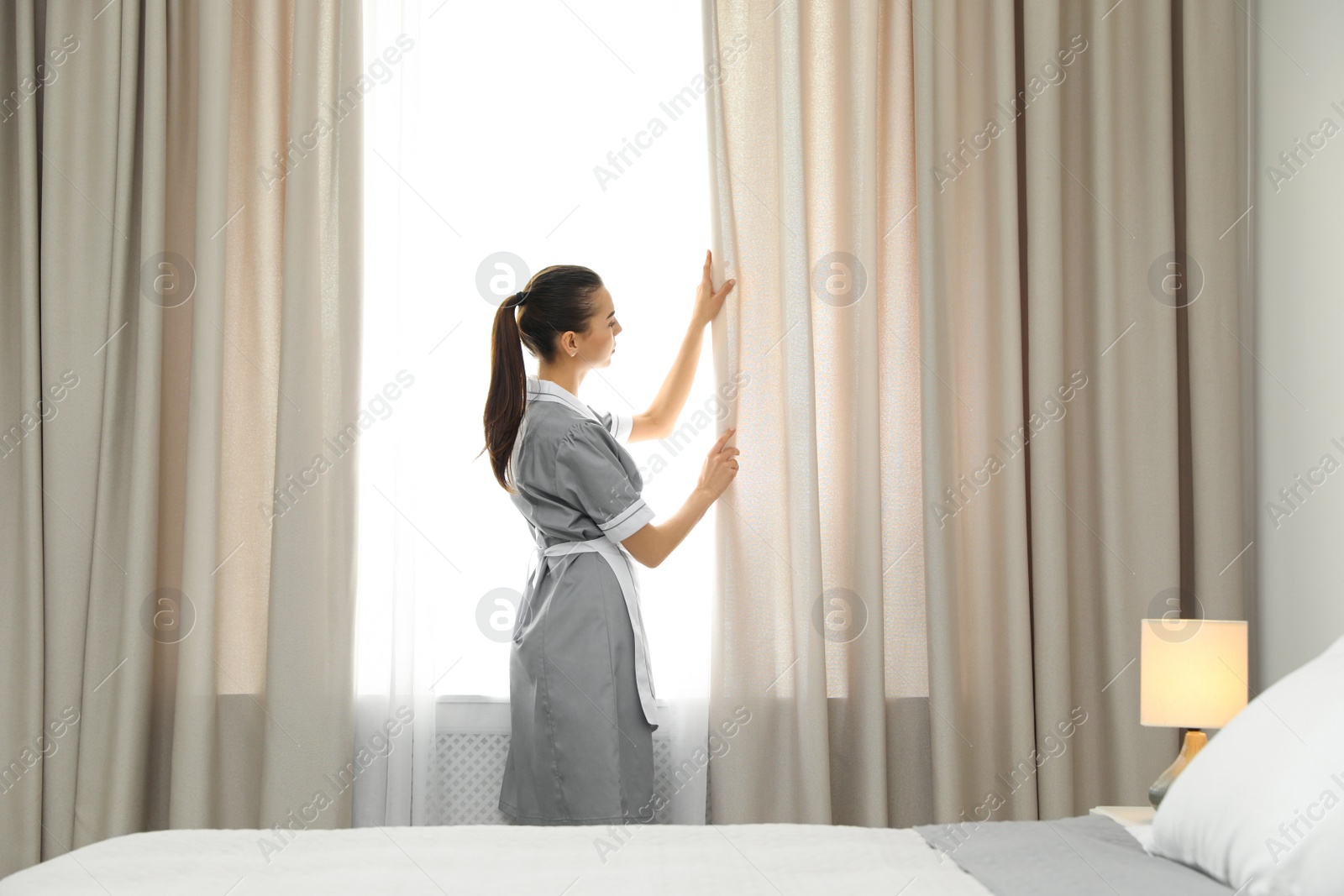 Photo of Chambermaid adjusting curtains in room. Hotel service