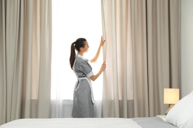 Chambermaid adjusting curtains in room. Hotel service