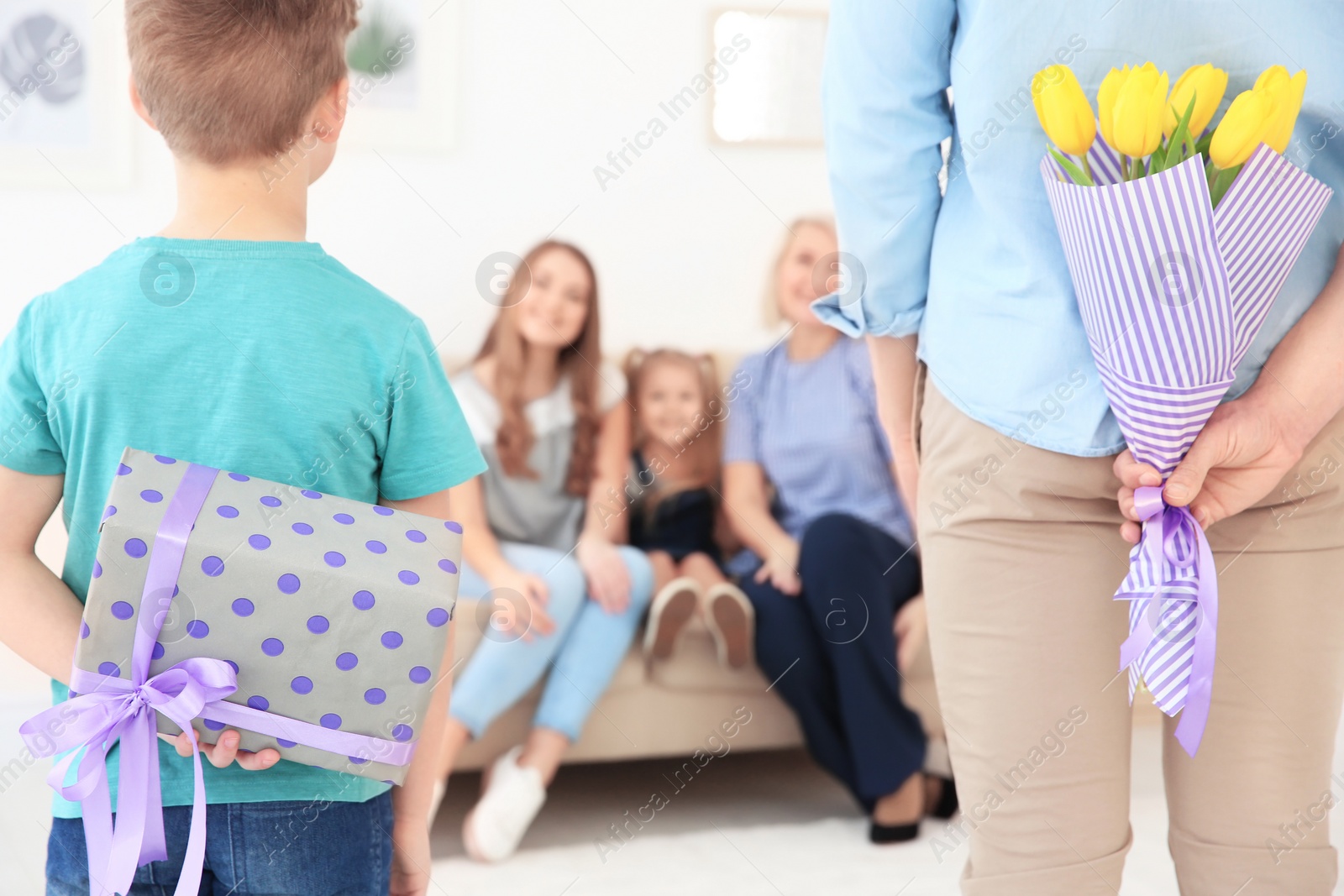 Photo of Little boy and his father hiding flowers and gift for women behind their backs at home