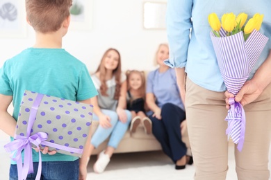 Little boy and his father hiding flowers and gift for women behind their backs at home