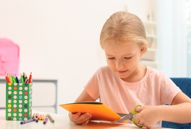 Little left-handed girl cutting construction paper at table