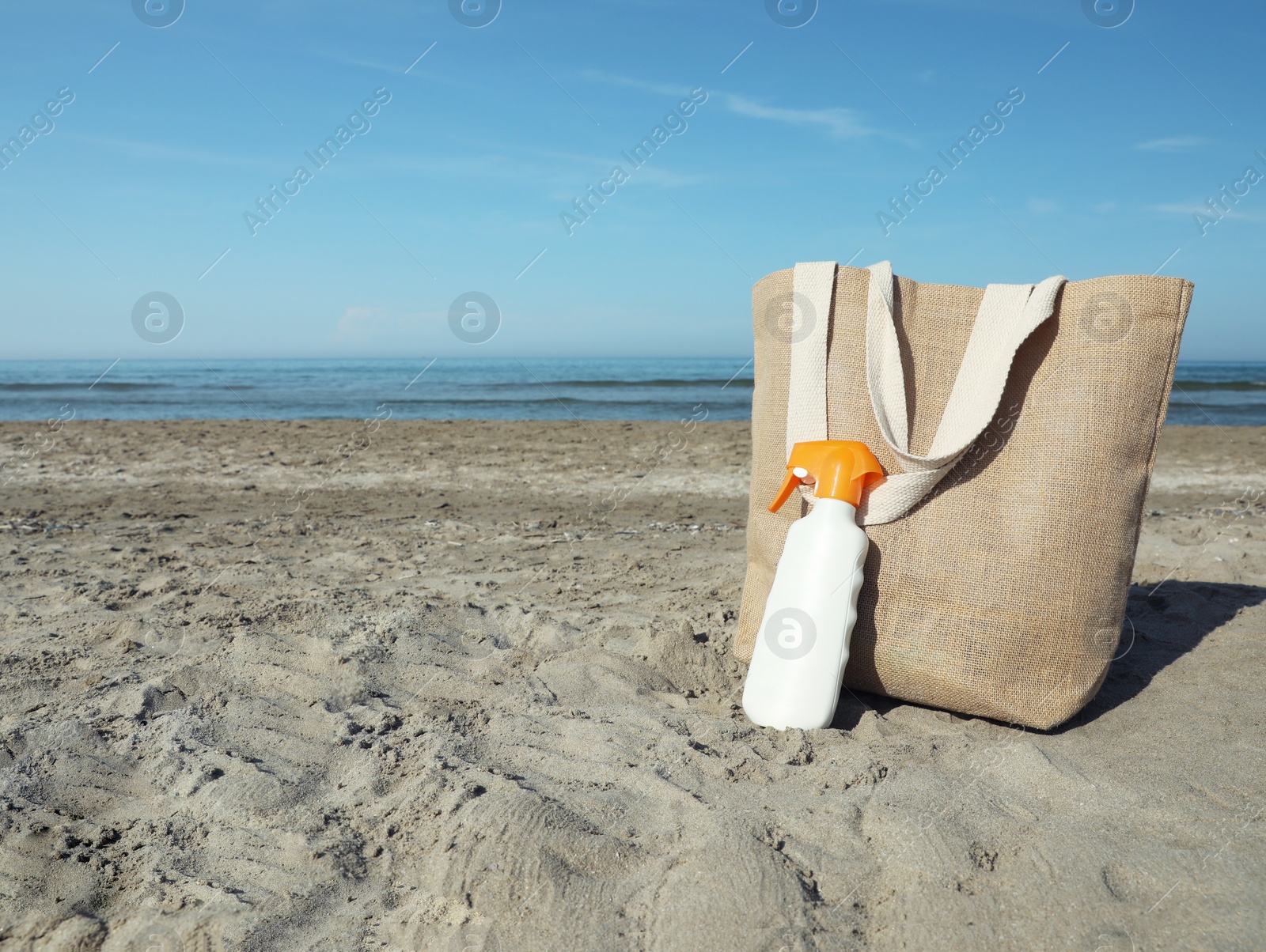 Photo of Bag and sun protection product on sandy beach. Space for text