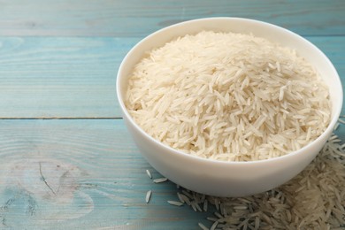 Photo of Raw basmati rice in bowl on light blue wooden table, space for text