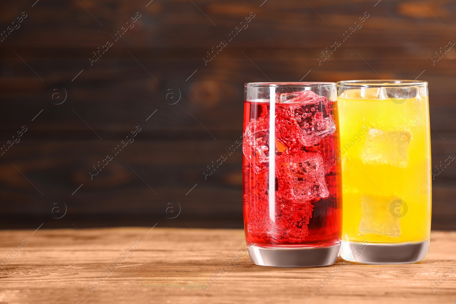 Photo of Glasses of different refreshing soda water with ice cubes on wooden table, space for text