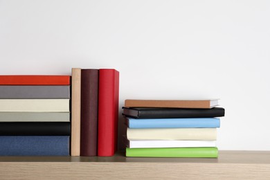 Photo of Many hardcover books on wooden table near white wall. Space for text