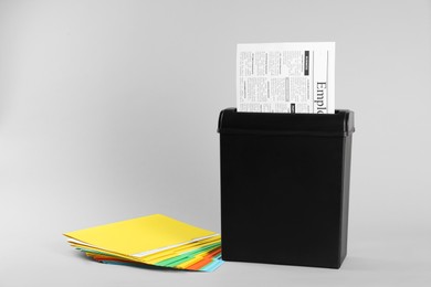 Shredder with sheet of paper and colorful folders on grey background. Space for text