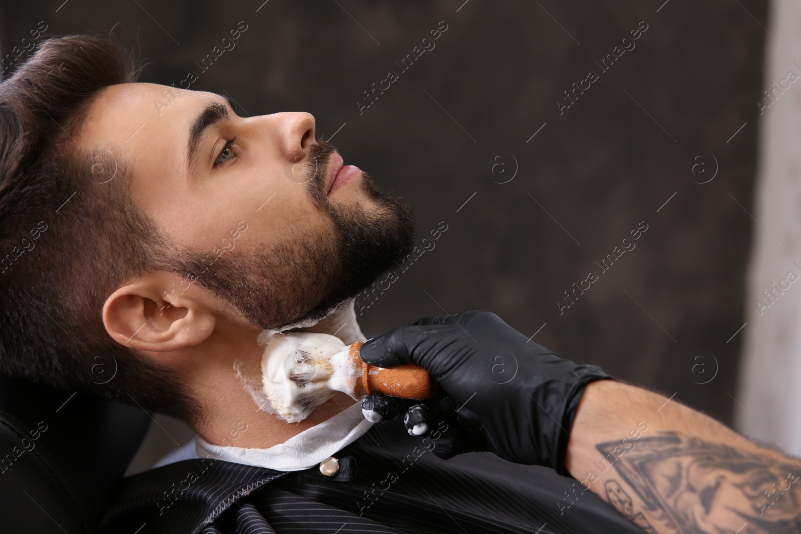 Photo of Professional hairdresser applying shaving foam onto client's skin in barbershop