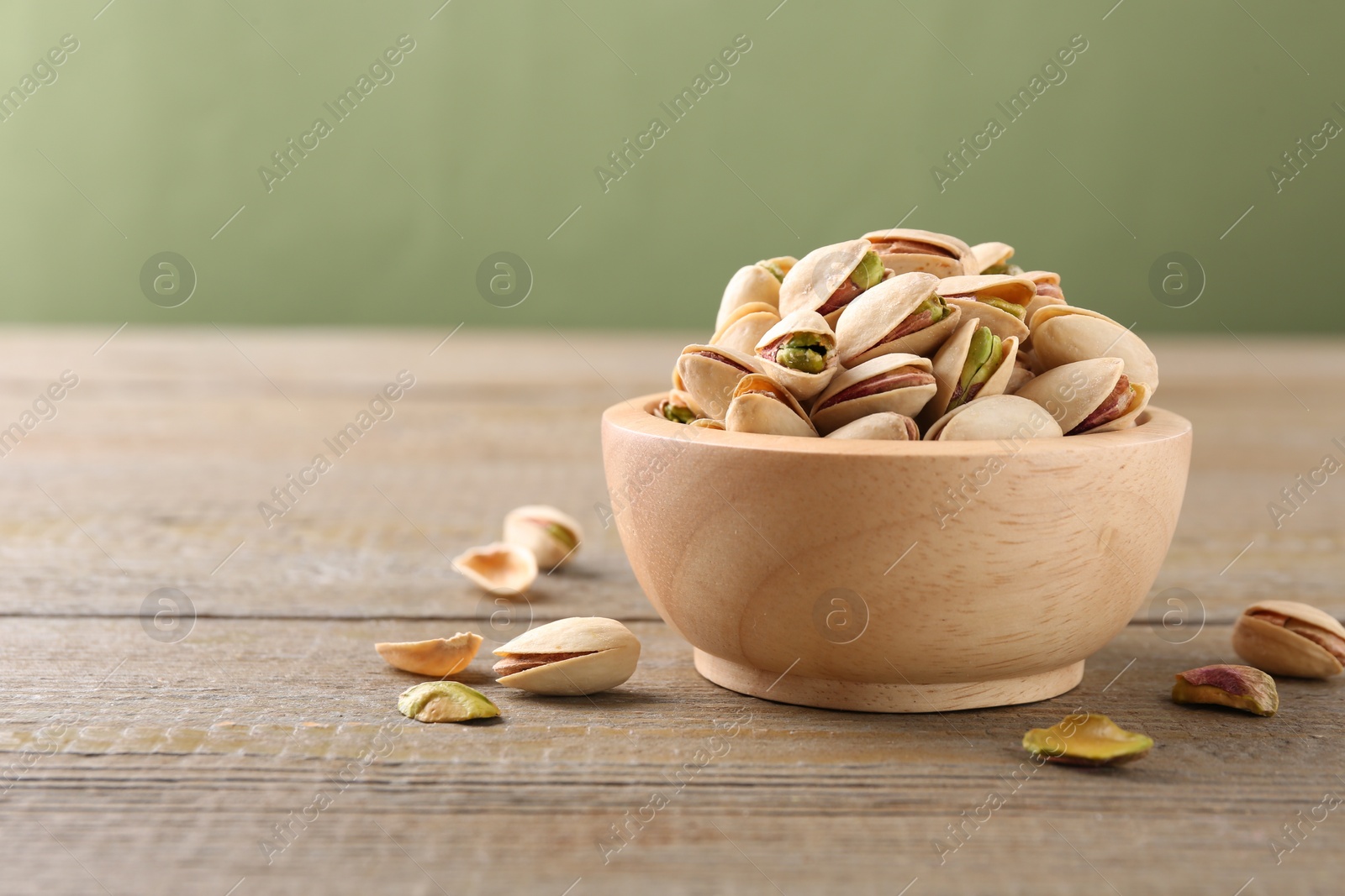 Photo of Tasty pistachios in bowl on wooden table against olive background, closeup. Space for text