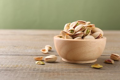 Tasty pistachios in bowl on wooden table against olive background, closeup. Space for text