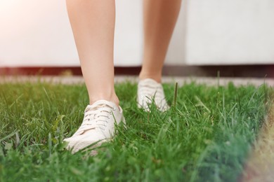 Photo of Woman in stylish sneakers walking on green grass outdoors, closeup. Space for text