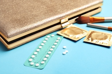 Photo of Birth control pills and condoms near clutch on light blue background. Safe sex concept