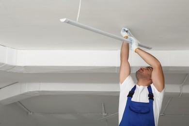 Photo of Electrician installing led linear lamp indoors, space for text. Ceiling light