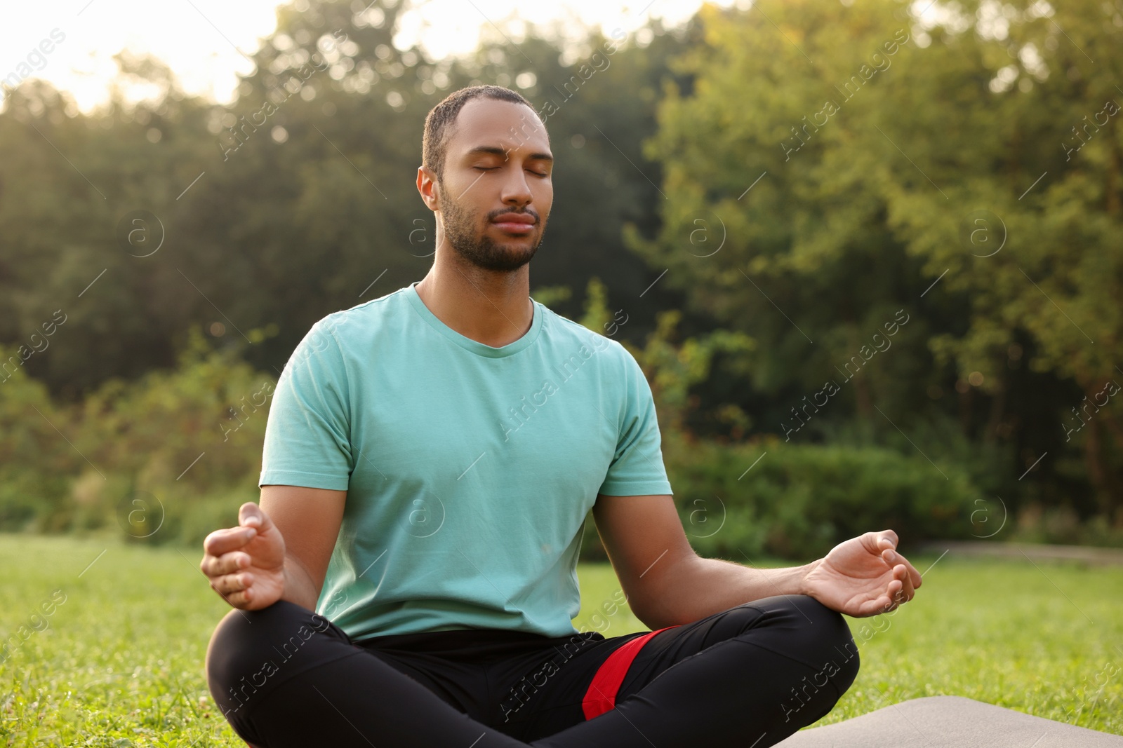 Photo of Man practicing yoga on mat outdoors. Lotus pose