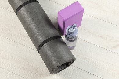 Photo of Exercise mat, yoga block and bottle of water on light wooden floor, above view