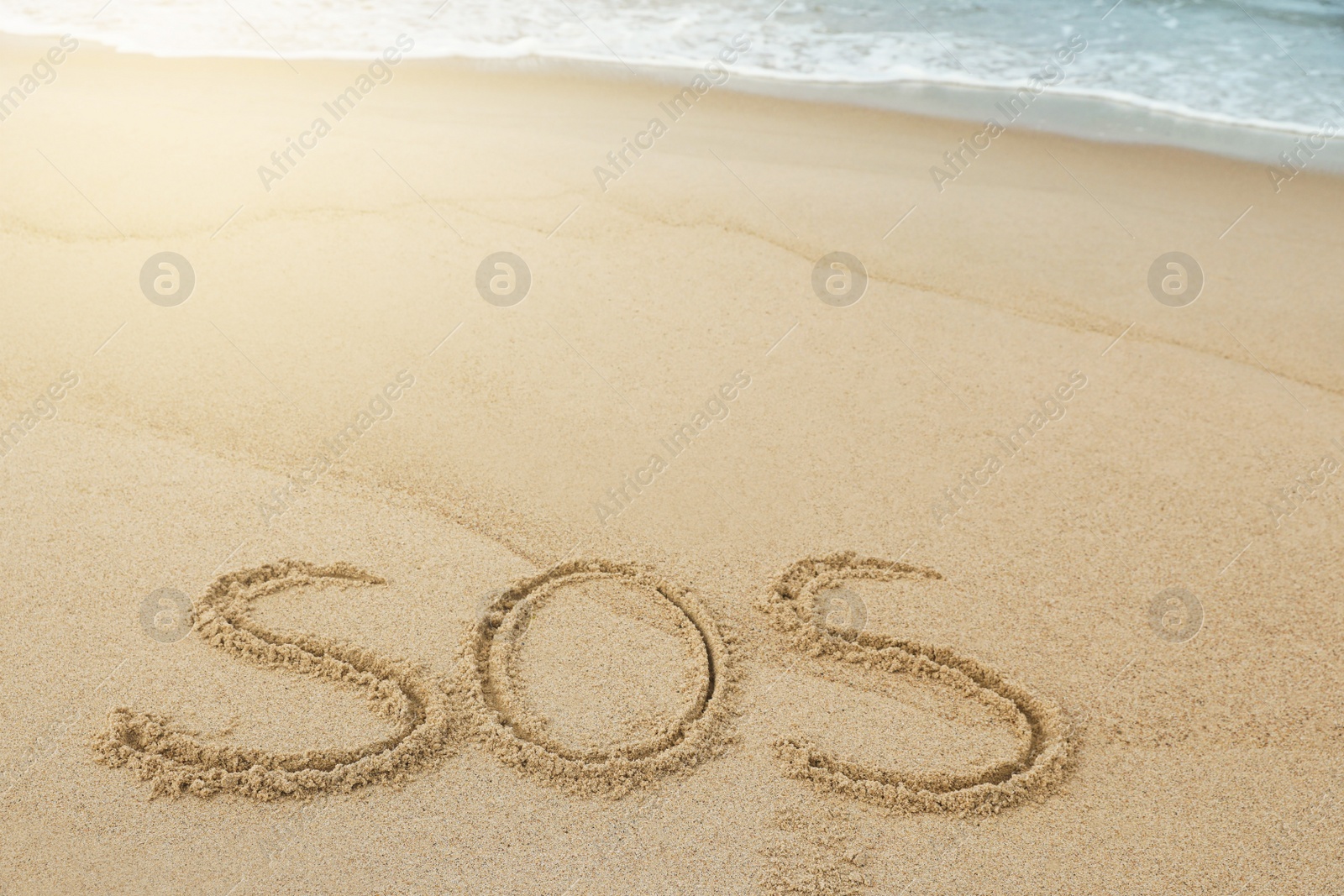 Photo of Message SOS drawn on sand near sea