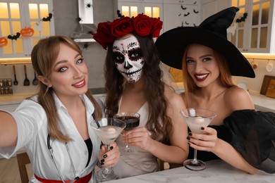 Group of women in scary costumes with cocktails taking selfie at Halloween party indoors