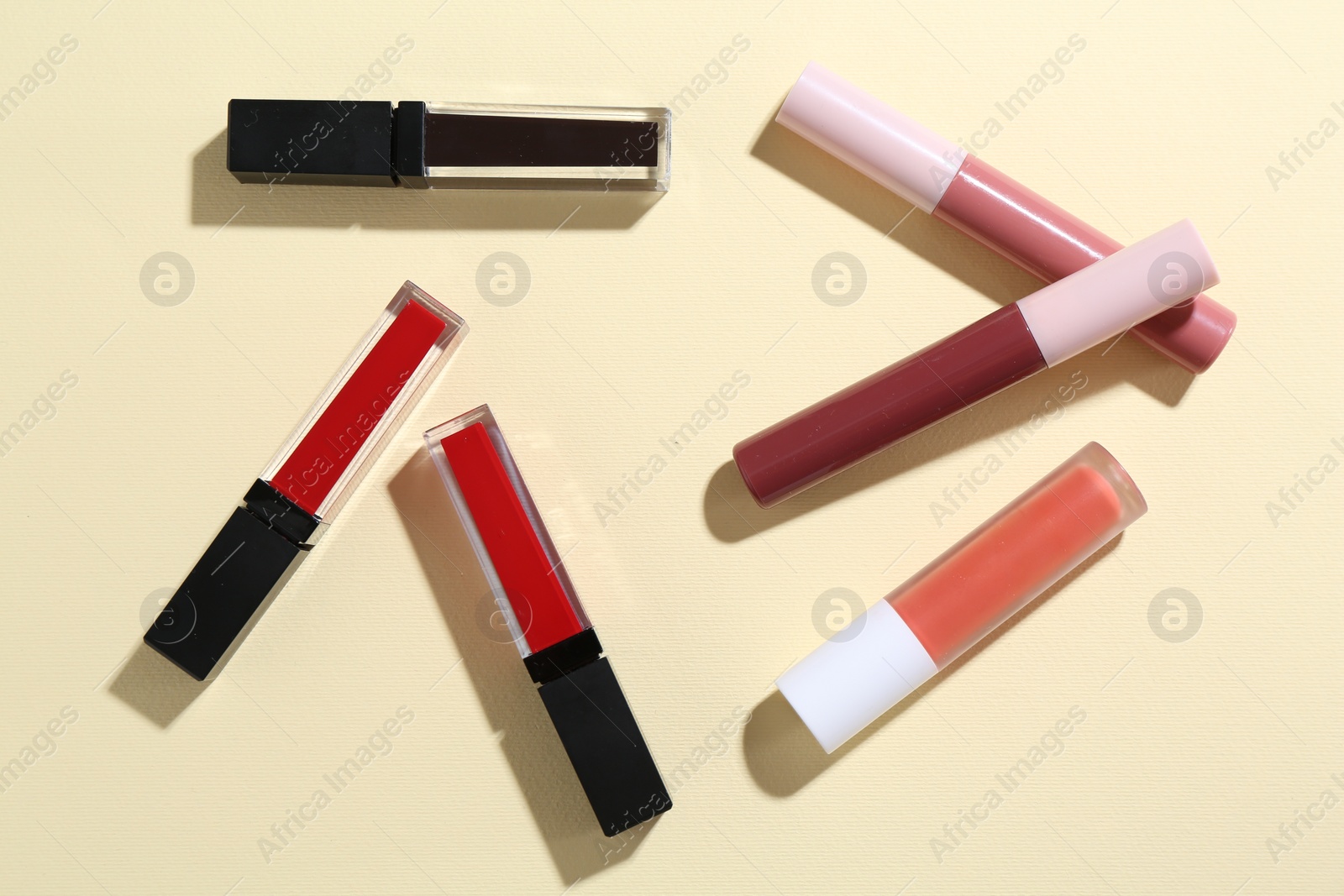 Photo of Different lip glosses on pale yellow background, flat lay