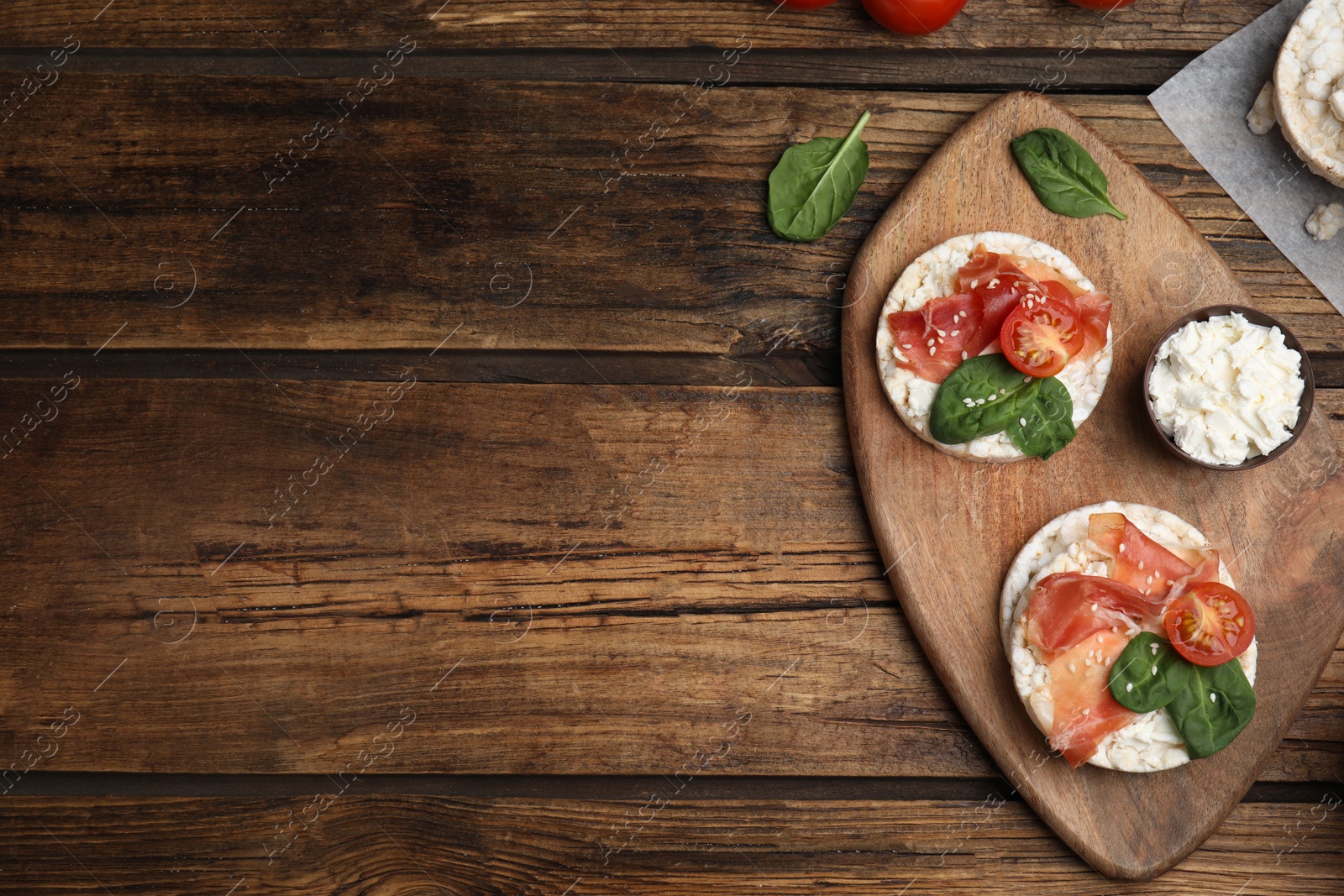 Photo of Puffed rice cakes with prosciutto, tomato and basil on wooden table, flat lay. Space for text