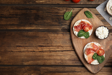 Photo of Puffed rice cakes with prosciutto, tomato and basil on wooden table, flat lay. Space for text