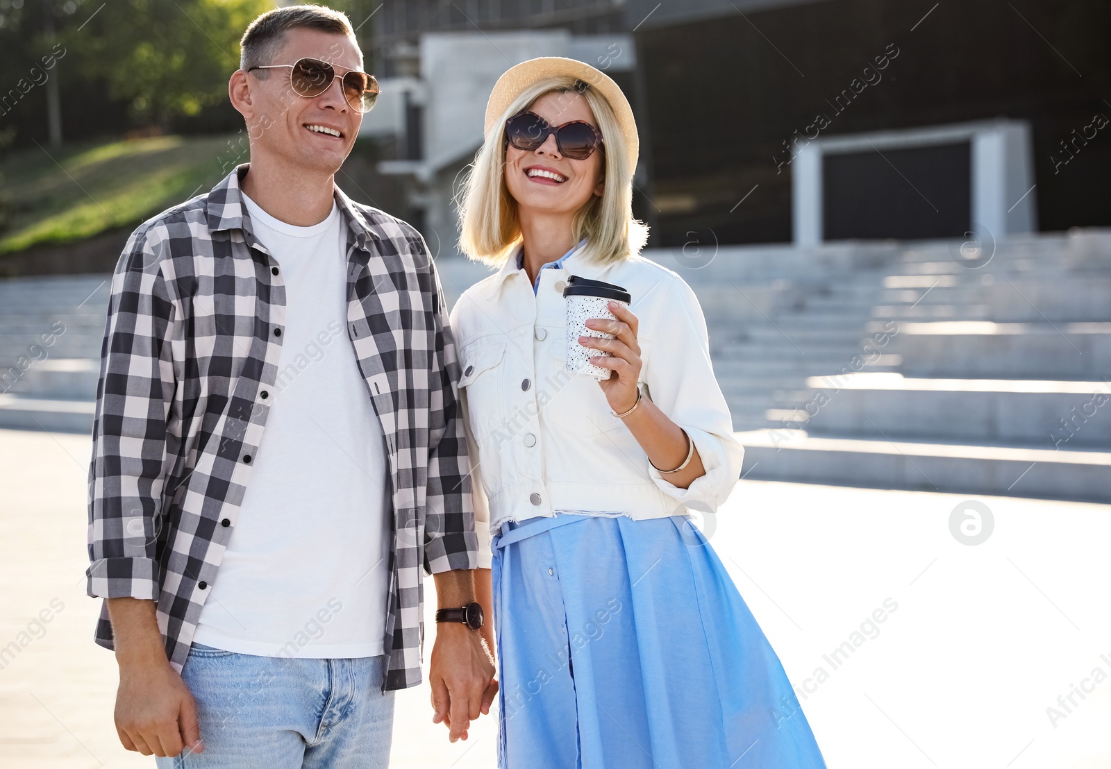 Photo of Happy couple with drink walking along city street on summer day