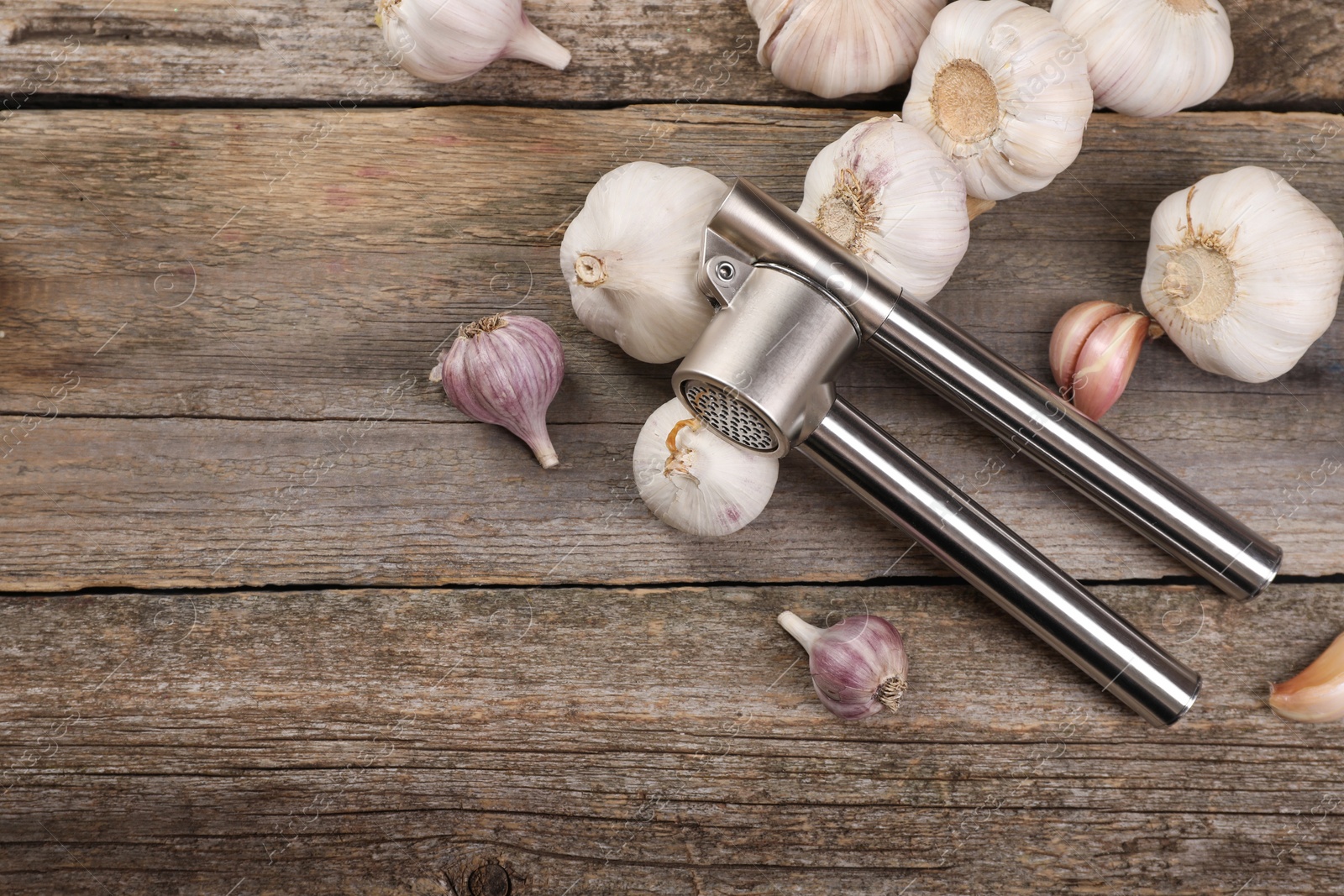 Photo of Garlic press and bulbs on wooden table, flat lay. Space for text
