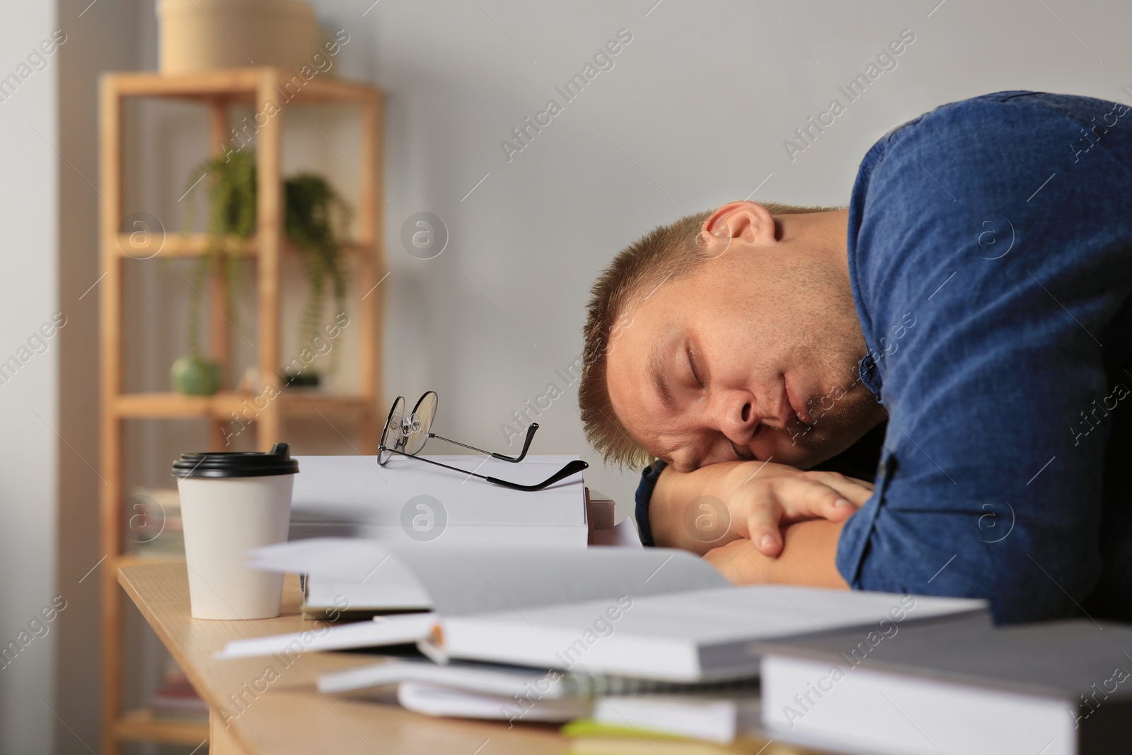 Photo of Tired man sleeping near books at wooden table indoors