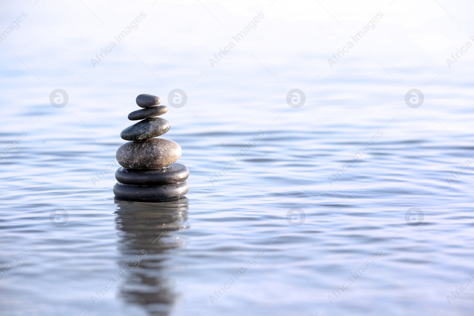 Photo of Stack of dark stones in sea water, space for text. Zen concept