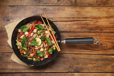 Photo of Stir-fry. Tasty noodles with meat in wok and chopsticks on wooden table, top view