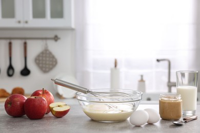 Whisk, bowl, beaten eggs and other ingredients on grey table indoors, space for text